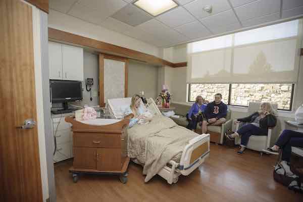 Mother holding newborn in a private room with people seated nearby Mother holding newborn in a private room with people seated nearby