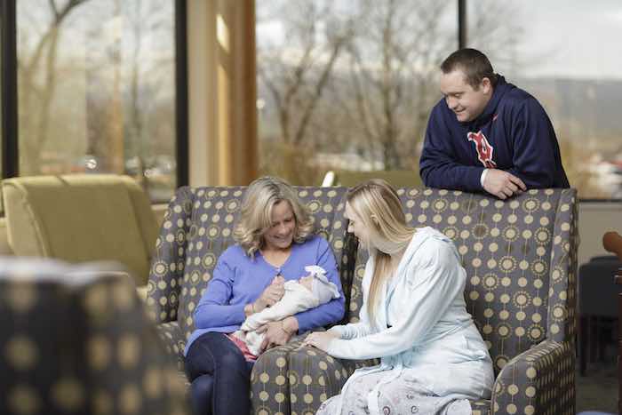 A woman sitting holding a newborn while two other people admire