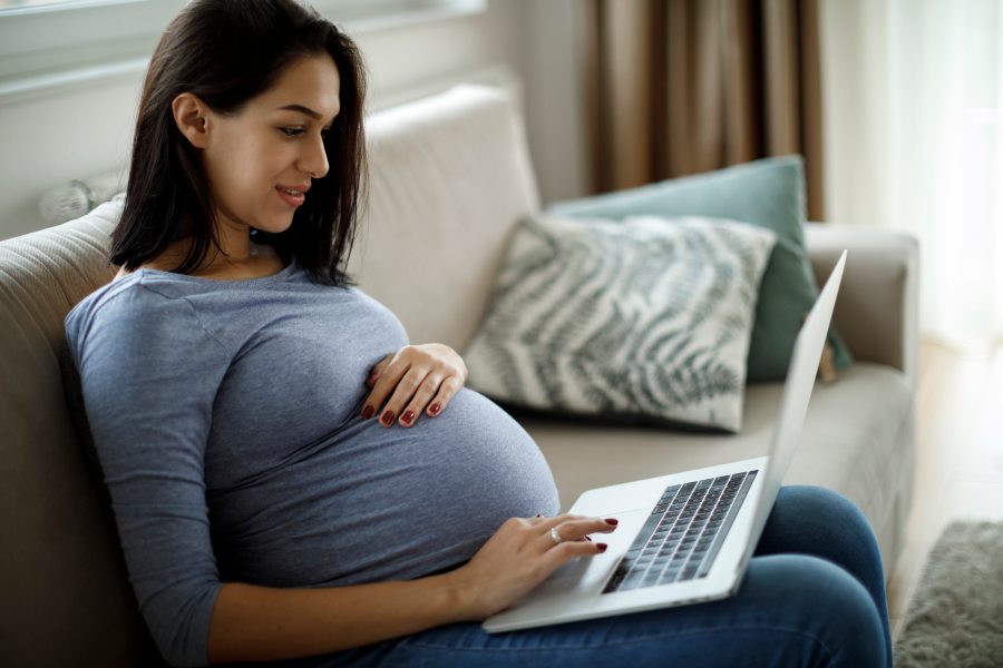 Childbirth Education A pregnant woman sitting on the couch reads a laptop screen