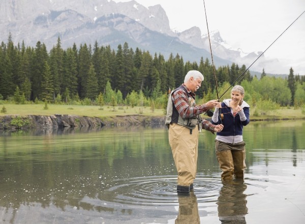 Fishing an older couple fishing in a stream with mountains in the background